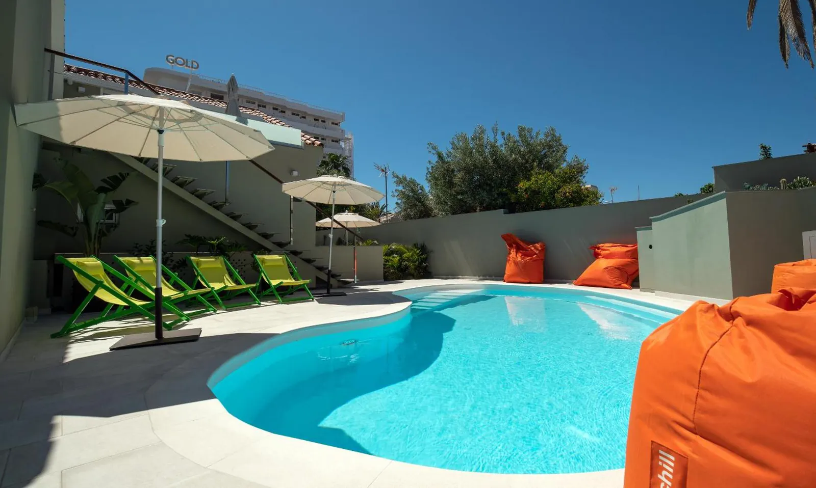 Kidney-shaped heated saltwater pool at Villa RG, with umbrellas and green loungers along the deck