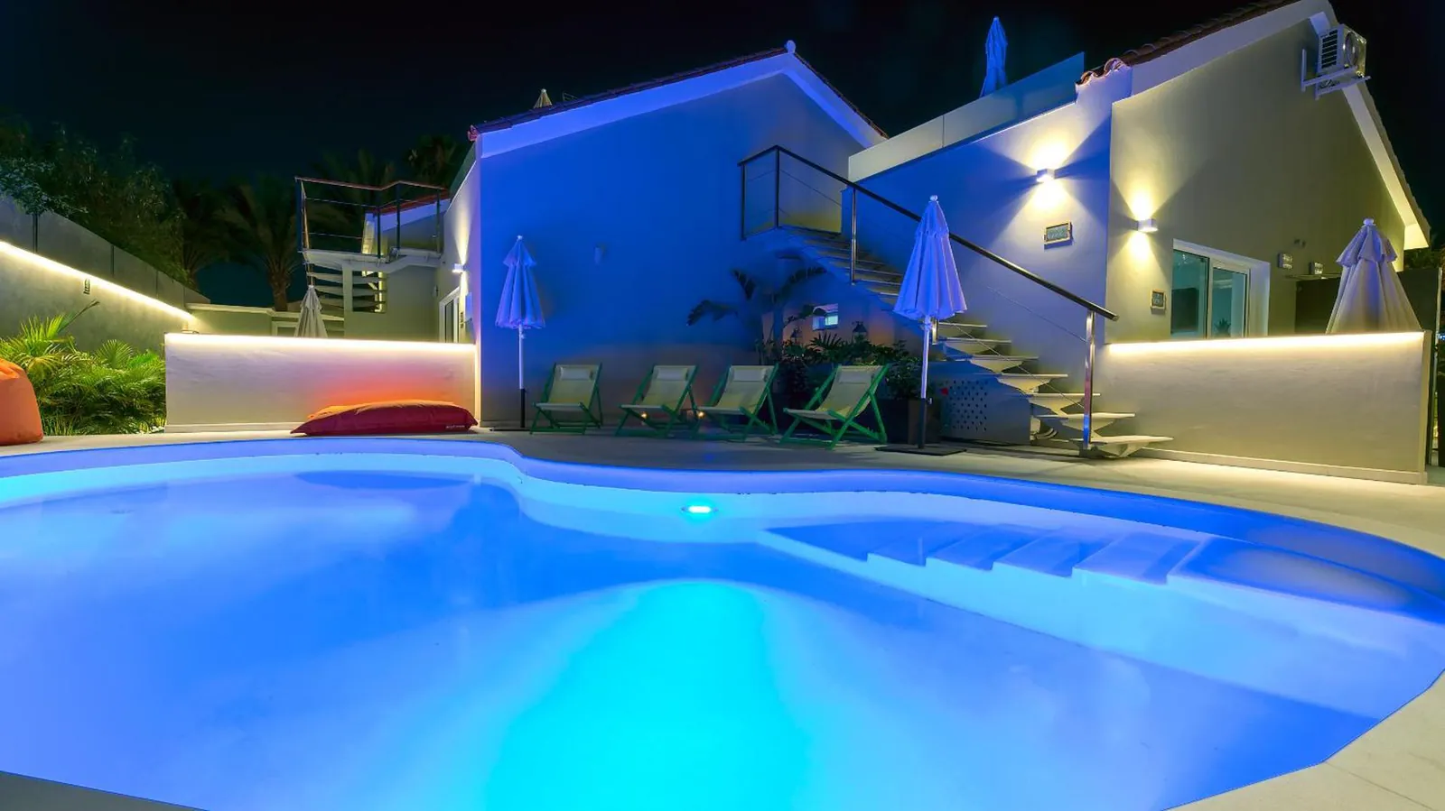 The pool lit blue after dark beside the white guest buildings