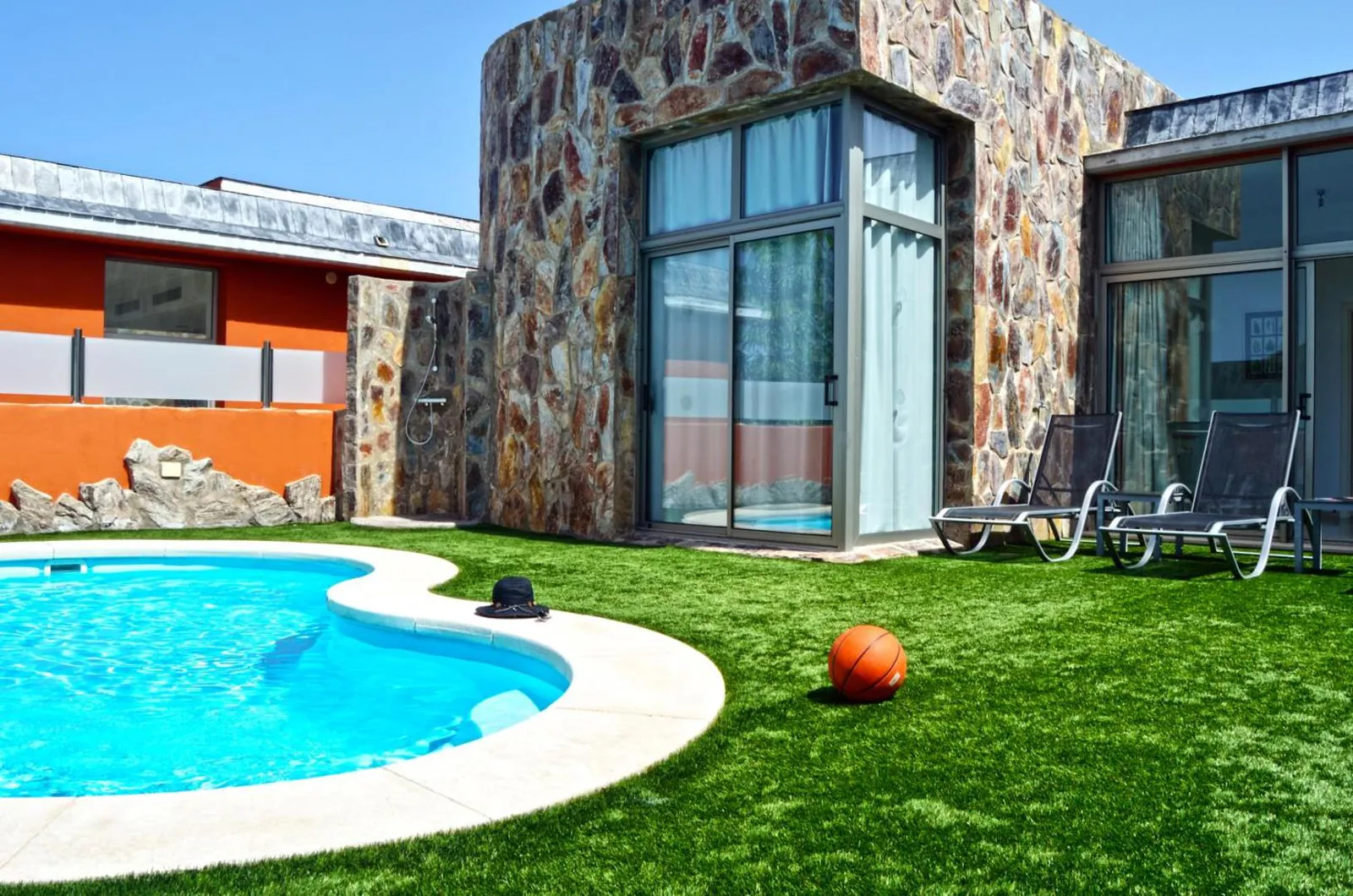 Curved private pool beside a stone-clad villa wall and lawn