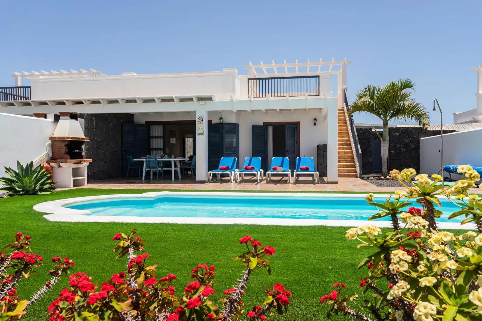 Private pool set into a lawn with flowering shrubs in front of a white villa at Villas Susaeta