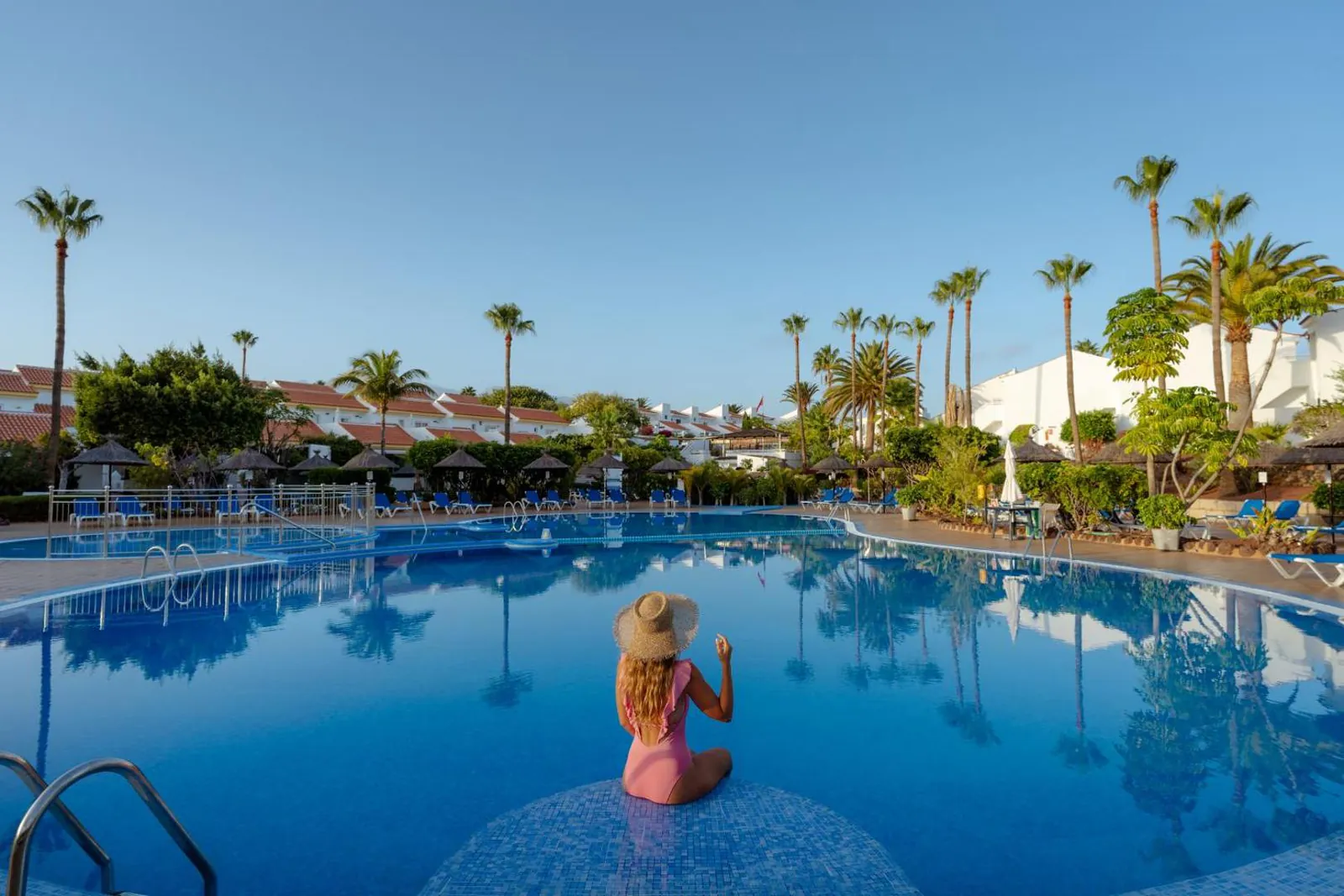Guest sitting in the main pool, lined with palms and the resort's white villas